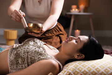 Woman undergoing singing bowl therapy lying on floor indoors