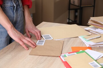 Woman putting barcodes onto envelopes at table in post office, closeup