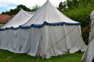 A view of a set of medieval tents made out of white cloth set up as a temporary camp during medieval fair in Poland, with an English flag, decorations, and useful items visible next to it 