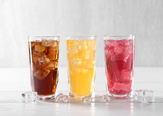 Soda water of different flavors in glasses with ice cubes on white wooden table