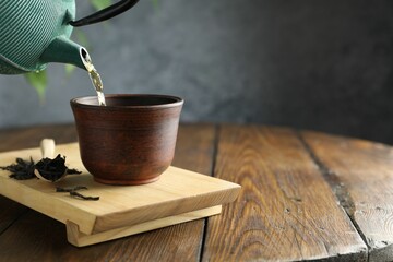 Pouring freshly brewed tea from teapot into cup at wooden table, closeup. Space for text