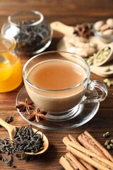Aromatic Masala tea in cup, spices, dry leaves and honey on wooden table, closeup