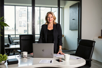 Confident Businesswoman Standing in Modern Office with Laptop and Documents