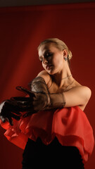 Fototapeta premium Portrait of sexy photo model posing in red dress and black transparent gloves. Luxurious girl on red background.