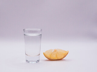 A glass of vodka and a slice of lemon, on a white background, front view