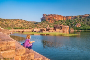 Woman exploring ancient ruins at Badami. Tourist sitting on lake shore relaxing at Badami temple, Karnataka, India