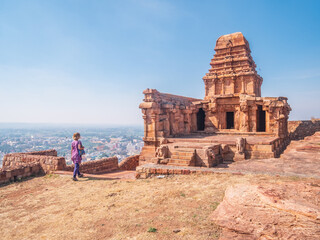 Woman exploring ancient temple site at Badami. Tourist walking among ruins stone walls gateways in Karnataka, India