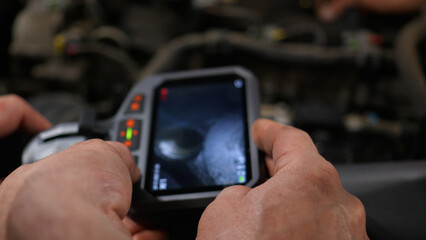 The mechanics at the auto service use an endoscope and examine the inside of the engine