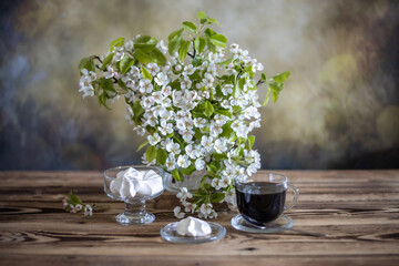 a cup of tea, marshmallows from aquafaba and branches of a blooming pear on a wooden table