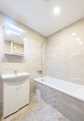 Modern Beige Tiled Bathroom with Bathtub and Sink in Bright Interior. Bright and stylish modern bathroom interior with beige tiles, bathtub, sink, and a mirror cabinet.