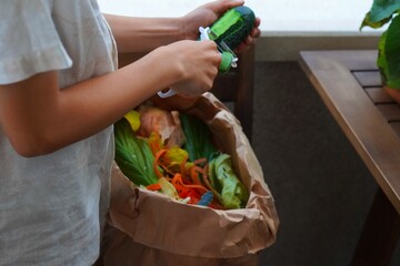 preteen boy peeling vegetables and depositing the scraps in the organic garbage to make compost
