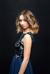Woman in blue dress with lace pattern posing in studio on dark background. Close-up portrait.