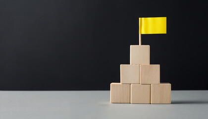 Stacked wooden cubes forming pyramid with yellow flag on top. Achievement, business success.
