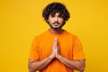 Young happy Indian man he wearing orange t-shirt casual clothes hold hands folded in prayer...