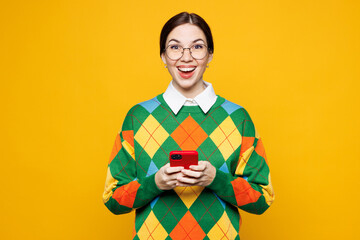 Young surprised shocked woman she wear glasses green sweater casual clothes hold in hand use mobile cell phone look camera isolated on plain orange yellow background studio portrait Lifestyle concept