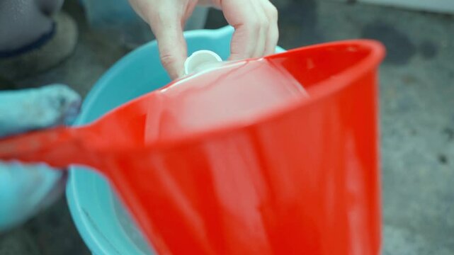 Pouring special liquid from a bucket into a spray bottle close-up, top view