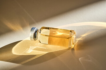Injection vial with medicinal product in sunlight on beige background.