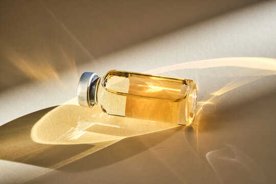 Injection vial with medicinal product in sunlight on beige background.