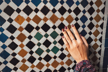 Woman's hand with dark nail polish gently touching an ornate wall covered in traditional moroccan zellige mosaic tiles