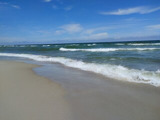 Dynamic Shoreline with Gentle Breaking Waves on Sandy Beach Under Bright Blue Sky and White Clouds