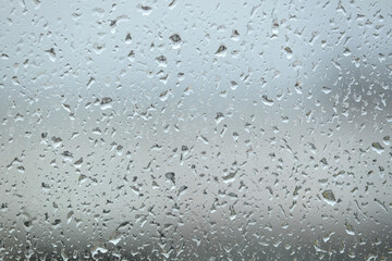 Background with rain drops are flowing down on window glass on blur gray background front view close up