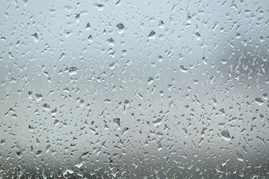 Background with rain drops are flowing down on window glass on blur gray background front view close up