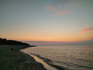 Obraz premium Serene Evening at Baltic Shoreline with Pink Sunset Sky Illuminating Coastal Curve and Creating Peaceful Atmosphere at Dusk