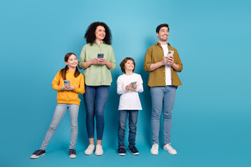 Obraz premium Happy family of four standing together holding smartphones showing cheerful expressions on a blue studio background
