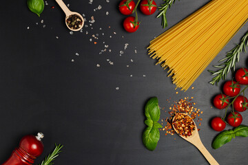 Dry spaghetti with spices, tomatoes and salt. On a black background. Free space for text . Top view