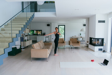 Young Beautiful Female Exercising, Stretching and Practising Yoga with Trainer via Video Call Conference in Bright Sunny House. Healthy Lifestyle, Wellbeing and Mindfulness Concept