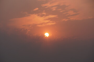 The sun is setting behind the clouds with the orangish sky background