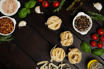 Uncooked pasta and vegetables cooking background, top view, copy space. Italian pasta, tomatoes, basil herbs and spices, italian cuisine concept.