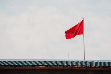 Red flag adorned with a green star waving proudly atop a rooftop in Morocco, symbolizing national...