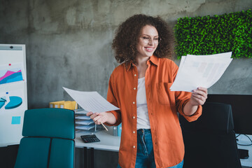Confident young businesswoman reviewing documents at the modern office workspace with a casual...