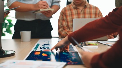 A group of professionals engages in a collaborative meeting, analyzing charts and data on a table, showcasing teamwork and modern office dynamics with technology. SACTR