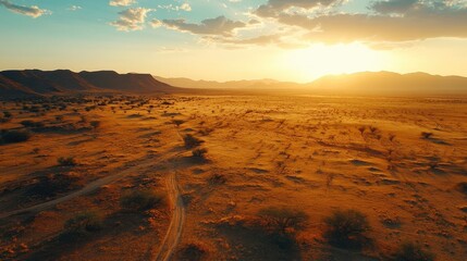 Naklejka premium Aerial View of Vast Desert Landscape at Sunset, Showing Rugged Terrain, Sparse Vegetation, and Distant Mountain Range, Golden Hour Light.