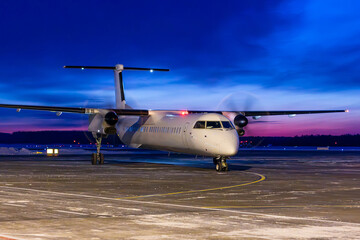 White passenger turboprop airliner taxiing through an airport at dawn