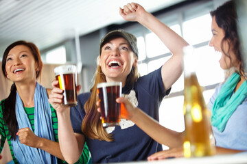 Pub, sports and fans cheering with beer watching soccer match with happiness for winning goal. Support, alcohol and group of friends streaming broadcast television of football game for league in bar.