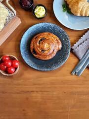 Several freshly baked croissants on a ceramic plate, next to a cup of coffee, a small jar of cream and jam. This image is suitable for cafe menus, food blogs, lifestyle magazines and culinary sites.