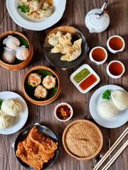 Image of various Chinese dim sum in a bamboo steamer, equipped with chopsticks and tea, on a wooden table. Perfect for illustrating Asian cooking articles, restaurant menus and food blog content.