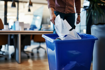 Person discarding paper into blue recycling bin in office environment