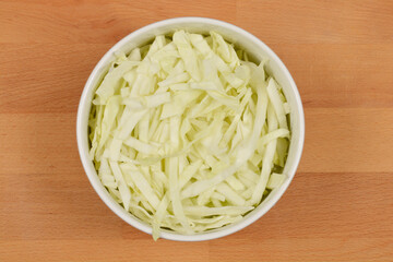 A top-down view of a white oval bowl filled with shredded white cabbage, set against a wooden...