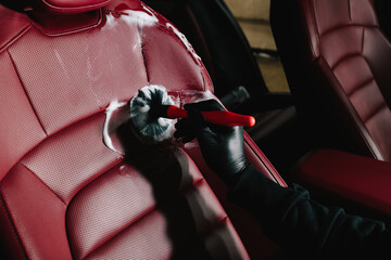 Car detailing process of cleaning leather auto seat with soap foam at the carwash. Man applies foam...