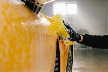 Procedure of washing car with soap solution and detergent before auto detailing. Worker cleans...