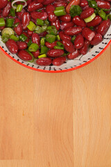 Red kidney bean salad with spring onions in a decorative bowl, shot from above on a wooden surface
