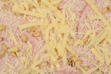 Close-up shot of an unbaked pizza with mortadella, cheese, and pine nuts, showcasing the ingredients and texture