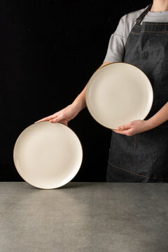 Young woman holding two white porcelain plates on black background