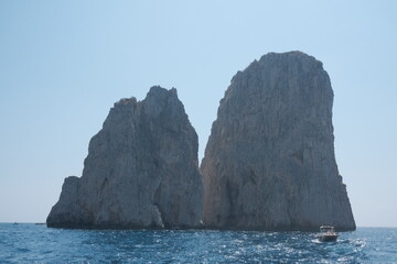 Fototapeta premium A boat sails in front of the iconic rock arch in Capri, Italy, with towering cliffs and crystal blue waters under a bright sky, showcasing the island’s dramatic coastal beauty.