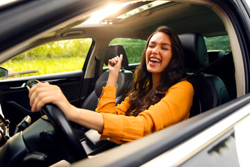 Overjoyed female driver enjoying auto ride, listening to music and singing while holding one hand...