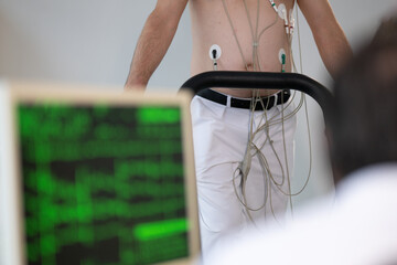 A middle-aged man is undergoing a medical stress test on a treadmill, connected to ECG electrodes...